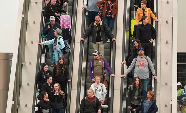 Travellers head down an escalator after clearing through a security checkpoint in Denver International Airport Friday, Nov. 7, 2025, in Denver. (AP Photo/David Zalubowski)