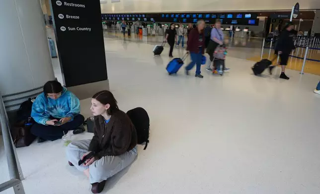 Grace Theodore, below center, and Isabel Azucena sit in a terminal at San Diego International Airport after learning their flight to New York was delayed by three hours Saturday, Nov. 8, 2025, in San Diego. (AP Photo/Gregory Bull)