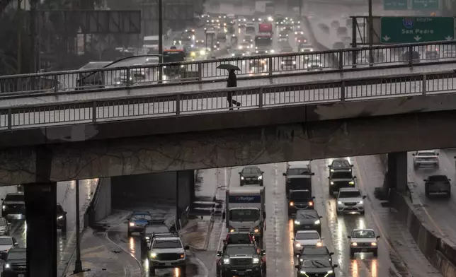 A pedestrian with an umbrella walks on a bridge over the rain-soaked 110 Freeway in Los Angeles Friday, Nov. 14, 2025. (AP Photo/Jae C. Hong)