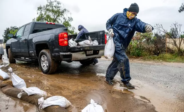 James Jones places a sandbag to prevent water from running off a property scorched in the Eaton Fire in Altadena, Calif., as the region remains under flash flood warnings on Saturday, Nov. 15, 2025. (AP Photo/Noah Berger)