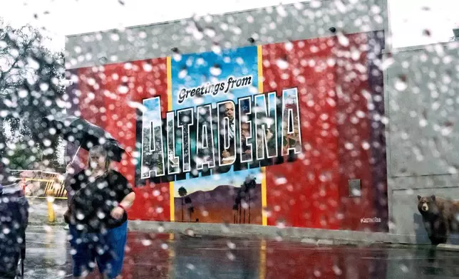A woman walks past a mural in Altadena, Calif., as the region remains under flash flood warnings Saturday, Nov. 15, 2025. (AP Photo/Noah Berger)