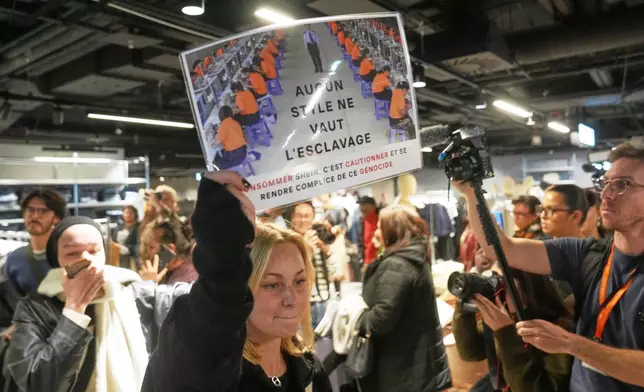 A protester holds a placard reading "No style worth slavery" in the BHV department store as fast fashion Shein opens its first physical store, Wednesday, Nov. 5, 2025 in Paris. (AP Photo/Thibault Camus)