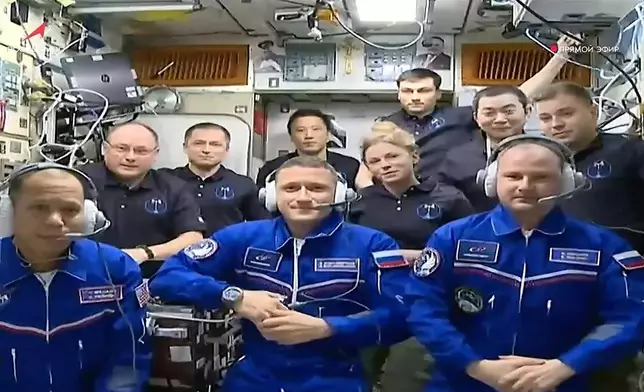 In this image, taken from video footage released by the Roscosmos Space Agency, newly arrived to the International Space Station, wearing blue suits, NASA astronaut Chris Williams, left, Roscosmos cosmonauts Sergey Kud-Sverchkov, center, and Sergey Mikaev pose among other participants of expedition to the International Space Station, after docking the Soyuz MS-28 spaceship to the station on Thursday, Nov. 27, 2025. (Roscosmos Space Agency via AP)