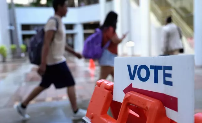 FILE - People walk past a "vote" sign on the first day of early voting in the general election in Miami, Oct. 21, 2024. (AP Photo/Lynne Sladky, File)