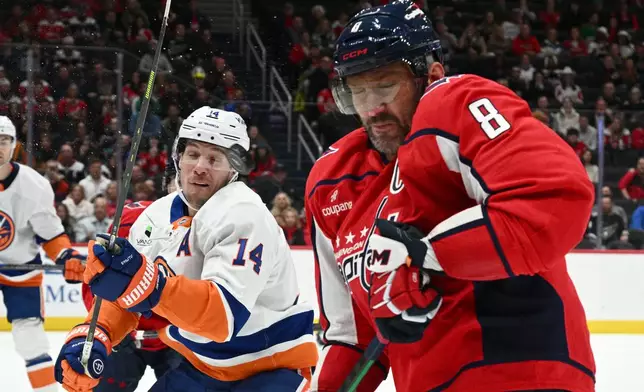 New York Islanders center Bo Horvat (14) and Washington Capitals left wing Alex Ovechkin (8) react to the flying puck during the first period of an NHL hockey game, Friday, Oct. 31, 2025, in Washington. (AP Photo/Nick Wass)