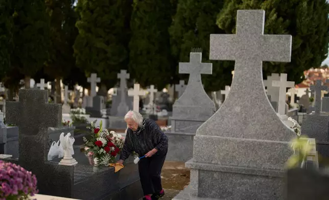 A woman cleans a grave on All Saints' Day, a Catholic holiday to reflect on the saints and deceased relatives, at the municipal cemetery in Campo Real, Spain, Saturday, Nov. 1, 2025. (AP Photo/Manu Fernandez)