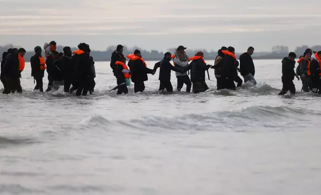 Migrants walk in the water to board a small boat in an attempt to reach Britain, Thursday, Nov. 6, 2025 in Gravelines, northern France. (AP Photo/Jean-Francois Badias)