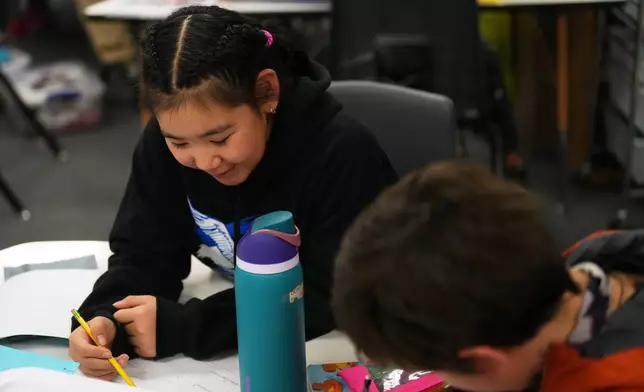 Rayann Martin, a 10-year-old displaced from the village of Kipnuk by ex-Typhoon Halong, left, talks with new classmate Lilly Loewen, 10, right, as they work in the Yup'ik language at College Gate Elementary, Thursday, Oct. 30, 2025, in Anchorage, Alaska. (AP Photo/Lindsey Wasson)