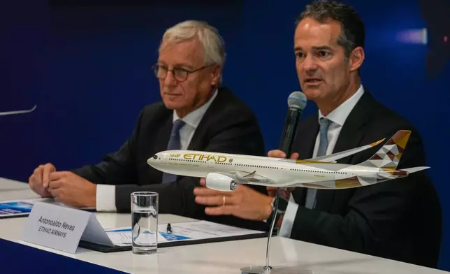 A model of Airbus A350 sits on the table as Etihad Airways CEO Antonoaldo Neves speaks while Airbus' CEO of commercial aircraft Christian Scherer, left, looks on during a press conference to announce deal to purchase 16 Airbus planes at the Dubai Air Show, United Arab Emirates, Tuesday, Nov. 18, 2025. (AP Photo/Altaf Qadri)
