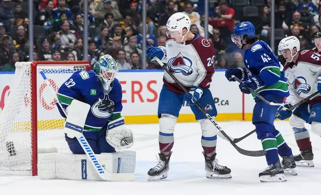 Vancouver Canucks goalie Kevin Lankinen (32) makes the save as teammate Quinn Hughes (43) and Colorado Avalanche's Ross Colton (20) and Gavin Brindley (54) watch during the second period of an NHL hockey game in Vancouver, B.C., Sunday, Nov. 9, 2025. (Darryl Dyck/The Canadian Press via AP)