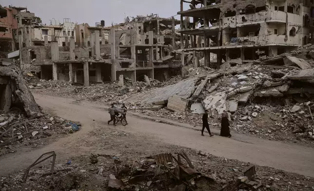Palestinians walk among the ruins of destroyed buildings in Gaza City Monday, Nov. 24, 2025. (AP Photo/Jehad Alshrafi)