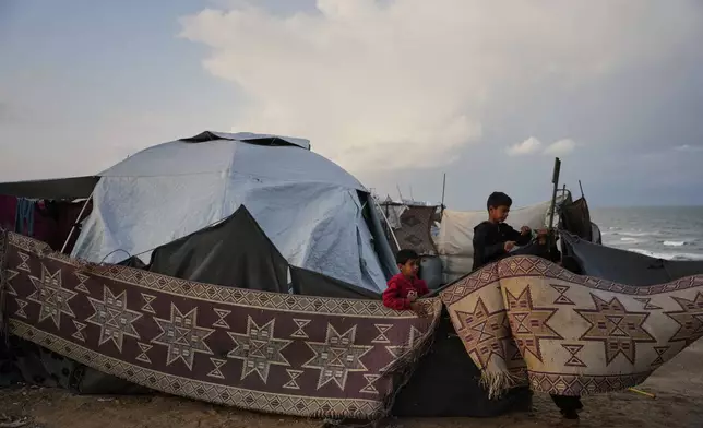 Fahd Al-Madhoun, 10, and his 7-year-old brother, Ziad, work to repair their family's tent after it was damaged by a storm at a temporary camp for displaced Palestinians on the beach in Deir al-Balah, in central Gaza, Tuesday, Nov. 25, 2025. (AP Photo/Abdel Kareem Hana)