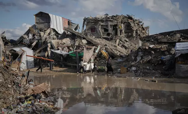 Palestinians walk among the ruins of destroyed buildings north of Gaza City Tuesday, Nov. 25, 2025. (AP Photo/Jehad Alshrafi)