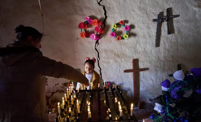 Nina Valentina Nieva helps her uncle Lorena Plaza light a candle in memory of her mother, Lorena Luca, inside a chapel at the cemetery during Day of the Dead celebrations in Susques, Jujuy province, Argentina, Saturday, Nov. 1, 2025. (AP Photo/Rodrigo Abd)