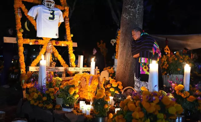 A woman stands next to the grave of a loved one celebrating the Day of the Dead at the cemetery of Tzintzuntzan, Michoacan state, Mexico, Friday, Oct. 31, 2025. (AP Photo/Eduardo Verdugo)
