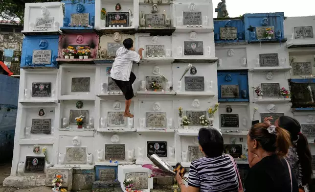 A man climbs apartment-type tombs at the hillside Barangka public cemetery in Marikina city, Philippines as people visit their loved ones during All Saints Day on Saturday, Nov. 1, 2025. (AP Photo/Aaron Favila)