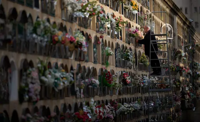 A man places flowers on a grave on All Saints' Day, a Catholic holiday to honor saints and remember deceased relatives, at a municipal cemetery in Barcelona, Spain, Saturday, Nov. 1, 2025. (AP Photo/Emilio Morenatti)