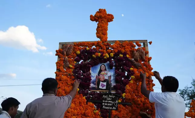 Relatives place flowers on an altar honoring Nayely Domingo Ceras during the Day of the Dead celebrations at the cemetery of Tzintzuntzan, Michoacan state, Mexico, Friday, Oct. 31, 2025. (AP Photo/Eduardo Verdugo)