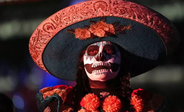 A girl dressed in a mariachi costume with skull makeup stands at the Zocalo, Mexico City's main square, ahead of the Day of the Dead, Friday, Oct. 31, 2025. (AP Photo/Claudia Rosel)