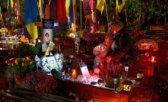 Relatives lit candles and bring flowers and flags at the graves of the Ukrainian soldiers who died in the war with Russia on All Saints' Day on the Mars Field at Lychakiv cemetery in Lviv, Ukraine, Friday, Oct. 31, 2025. (AP Photo/Mykola Tys)