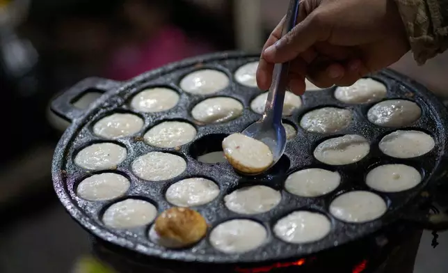 A vendor flips coconut-milk cakes known locally as khanom krok, a traditional sweet popular with both tourists and local residents, on a cast-iron pan at a morning market in Luang Prabang, Laos, Friday, Nov. 7, 2025. (AP Photo/Eugene Hoshiko)