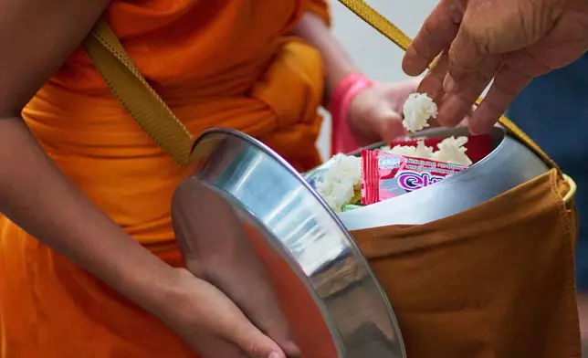 A novice Buddhist monk receives sticky rice as alms early morning in Luang Prabang, Laos, Friday, Nov. 7, 2025. (AP Photo/Eugene Hoshiko)