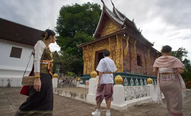 Visitors wearing traditional Lao dress arrive at a gilded Buddhist temple in Luang Prabang, Laos, to pay respects and explore the historic complex on Sunday, Nov. 2, 2025. (AP Photo/Eugene Hoshiko)