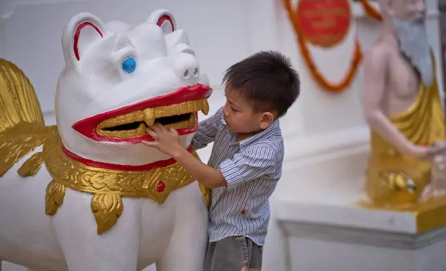 A child plays with a temple guardian statue outside a Buddhist temple in Luang Prabang, Laos, Sunday, Nov. 2, 2025. (AP Photo/Eugene Hoshiko)