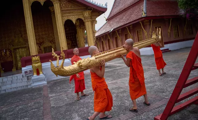 Novice Buddhist monks carry a gilded naga, a mythical serpent in Lao and Buddhist tradition, across the courtyard of a Buddhist temple in Luang Prabang, Laos, after a routine religious ceremony Wednesday, Nov. 5, 2025. (AP Photo/Eugene Hoshiko)