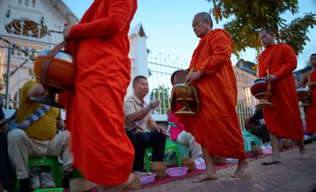 Buddhist monks walk in a line seeking alms from residents and tourists waiting along a street in Luang Prabang, Laos, Friday, Nov. 7, 2025. (AP Photo/Eugene Hoshiko)
