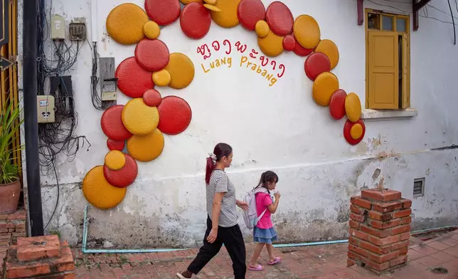Locals walk past a decorated wall in the UNESCO World Heritage city of Luang Prabang, Laos Wednesday, Nov. 5, 2025. (AP Photo/Eugene Hoshiko)