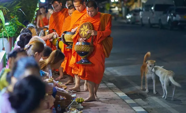 Buddhist monks walk in a line seeking alms from residents and tourists waiting along a street before dawn in Luang Prabang, Laos, Friday, Nov. 7, 2025. (AP Photo/Eugene Hoshiko)