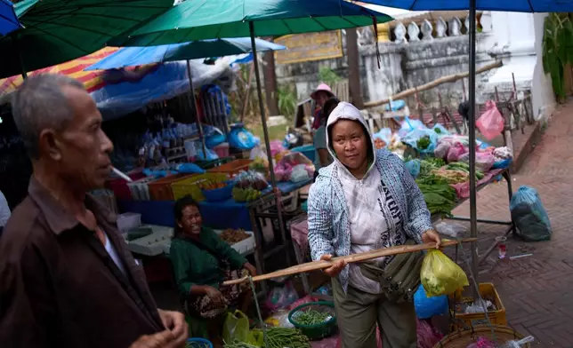 A vendor carries fresh produce with a shoulder pole through the bustling post-dawn morning market in Luang Prabang, Laos, as local residents shop for daily necessities, Sunday, Nov. 2, 2025. (AP Photo/Eugene Hoshiko)