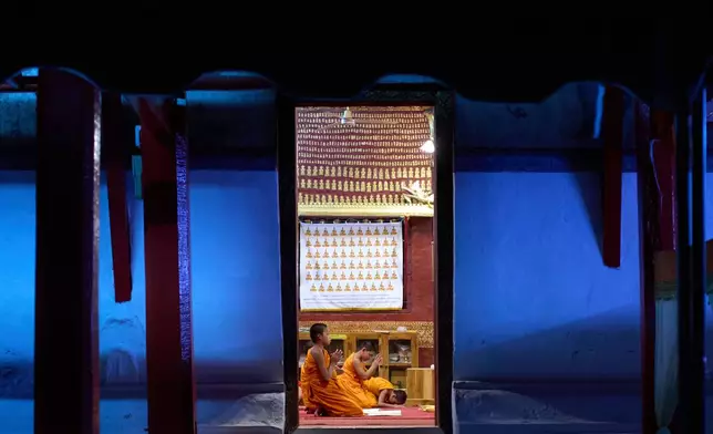 Novice Buddhist monks pray inside a temple as evening light fades outside in Luang Prabang, Laos, Sunday, Nov. 2, 2025. (AP Photo/Eugene Hoshiko)