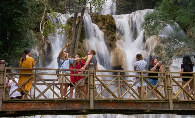 Tourists pose for photos on a footbridge in front of Kuang Si Waterfall near Luang Prabang, Laos, one of the country's most popular natural attractions known for its multi-tiered limestone cascades and turquoise pools on Tuesday, Nov. 4, 2025. (AP Photo/Eugene Hoshiko)