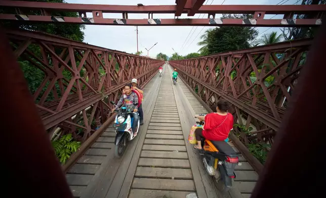Motorcyclists cross the Old French Bridge, a French colonial-era steel truss bridge that remains a key local crossing over the Nam Khan River in Luang Prabang, Laos, Wednesday, Nov. 5, 2025. (AP Photo/Eugene Hoshiko)