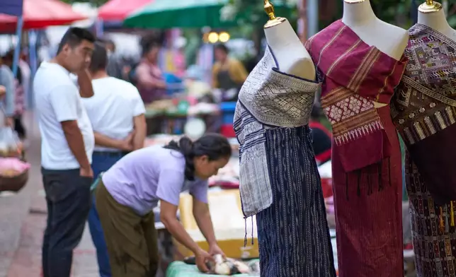 Traditional Lao outfits are displayed on mannequins as vendors and shoppers move through the night market in Luang Prabang, Laos, Monday, Nov. 3, 2025. (AP Photo/Eugene Hoshiko)