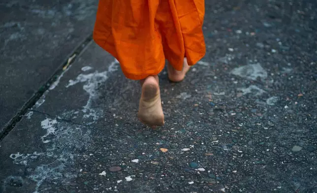 A novice Buddhist monk walks barefeet seeking alms early morning in Luang Prabang, Laos, Tuesday, Nov. 4, 2025. (AP Photo/Eugene Hoshiko)