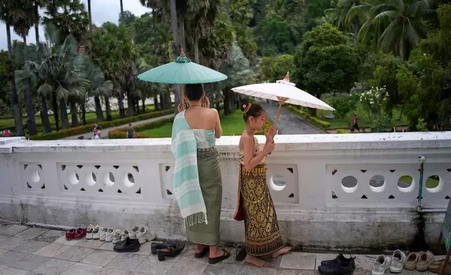A woman and a young girl wearing traditional formal Lao dress stand barefoot as they hold parasols on a temple terrace in Luang Prabang, Laos, Sunday, Nov. 2, 2025. (AP Photo/Eugene Hoshiko)