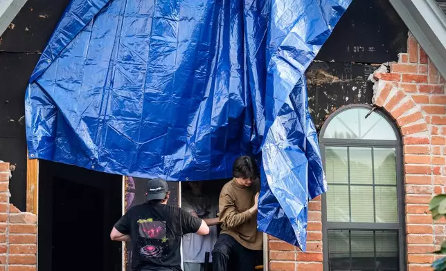 Aidan Bartlow, inside window, helps install a tarp on a storm damaged home after severe weather hit in the Memorial Northwest subdivision, in Spring, Texas, Monday, Nov. 24, 2025. (Brett Coomer/Houston Chronicle via AP)