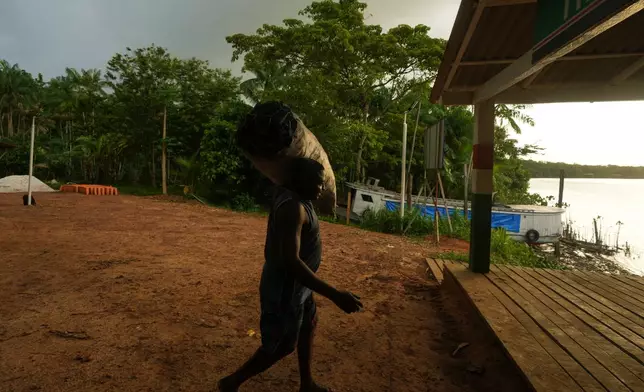 A man carries a charcoal sack to the harbor in Itacoa Miri, Brazil, Tuesday, Nov. 18, 2025, to be shipped for sale in Belem. (AP Photo/Fernando Llano)