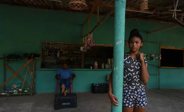 A girl stands next to her father in a grocery shop in Itacoa Miri, Brazil, Tuesday, Nov. 18, 2025. (AP Photo/Fernando Llano)