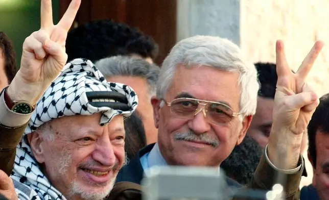 FILE.- Palestinian leader Yasser Arafat makes the victory sign as he leaves the confidence vote session of the Palestinian Legislative Council accompanied by Prime Minister-designate Mahmoud Abbas, right, at his headquarters in the West Bank town of Ramallah Tuesday, April 29, 2003. (AP Photo/Ricardo Mazalan, File)