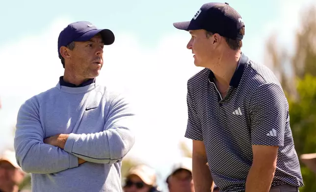 Rory McIlroy of Northern Ireland, left, speaks to Matt McCarty of the U.S., right, during the fourth round of the Australian Open golf tournament in Melbourne, Australia, Sunday, Dec. 7, 2025. (AP Photo/Asanka Brendon Ratnayake)
