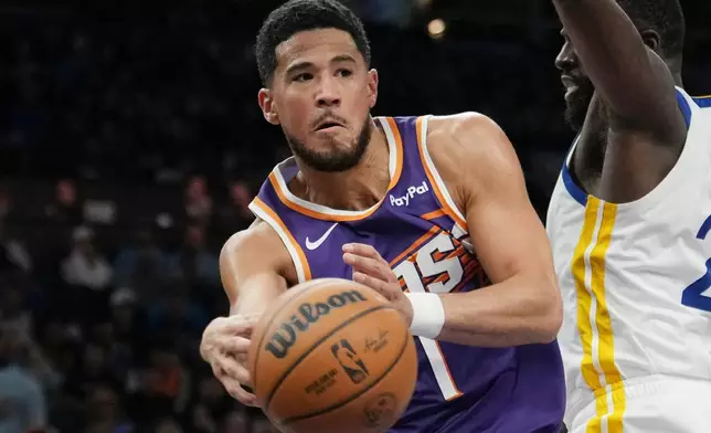 Phoenix Suns guard Devin Booker, left, gets off a pass against Golden State Warriors forward Draymond Green during the second half of an NBA basketball game Thursday, Dec. 18, 2025, in Phoenix. (AP Photo/Ross D. Franklin)