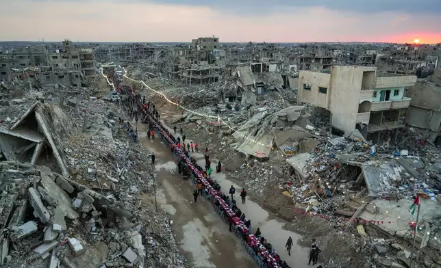 Palestinians sit at a large table surrounded by the rubble of destroyed homes and buildings as they gather for iftar, the fast-breaking meal, as the sun sets, on the first day of Ramadan, in Rafah, southern Gaza Strip, March 1, 2025. (AP Photo/Abdel Kareem Hana, File)