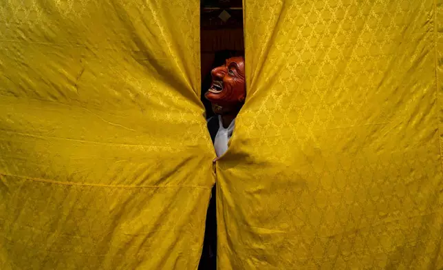 A masked monk stands behind a curtain, assisting a dancer in preparing for a traditional performance, during Gyalpo Losar, the Sherpa community's New Year celebration, at Shechen Monastery, in Kathmandu, Nepal, Feb. 25, 2025. (AP Photo/Niranjan Shrestha, File)