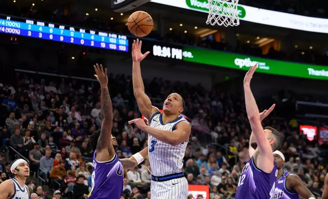 Orlando Magic guard Desmond Bane, center, lays up the ball to the basket over Utah Jazz forward Brice Sensabaugh, center left, during the first half of an NBA basketball game, Saturday, Dec. 20, 2025, in Salt Lake City. (AP Photo/Tyler Tate)