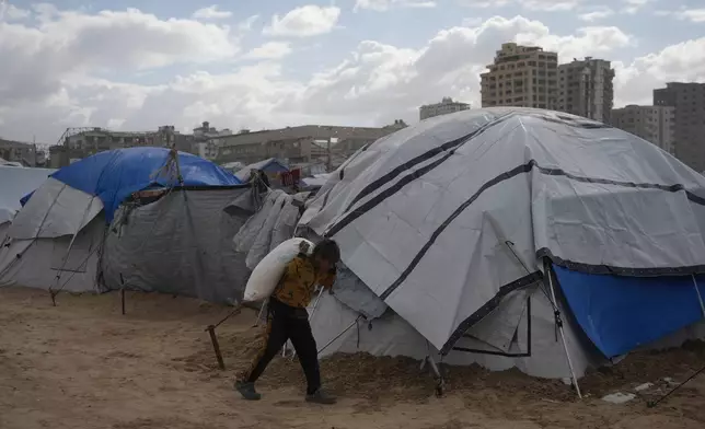 A Palestinian child carries a bag of flour on his back at a makeshift camp on the beach, in Gaza City, Sunday, Dec. 28, 2025. (AP Photo/Jehad Alshrafi)