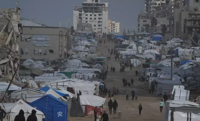 Palestinians walk along a street lined with war-damaged buildings in the rain, in Gaza City, Sunday, Dec. 28, 2025. (AP Photo/Jehad Alshrafi)